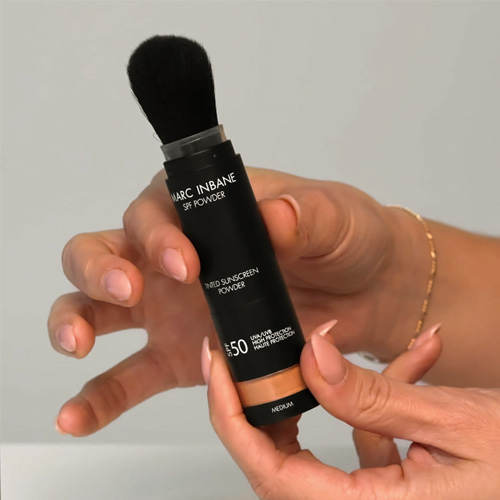 Een hand die de Marc Inbane Tinted Sunscreen Powder huls vasthoudt, wat een goed beeld geeft van het formaat en de luxe uitstraling van het product.