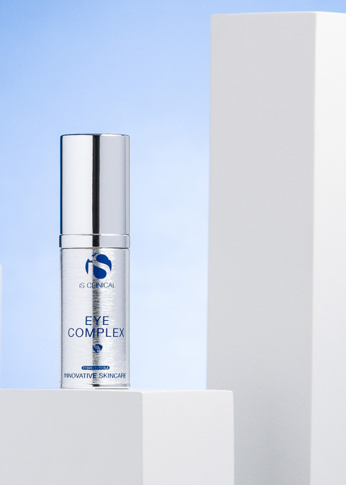 Een flesje iS Clinical Eye Complex staand op een wit blok tegen een lichtblauwe achtergrond.