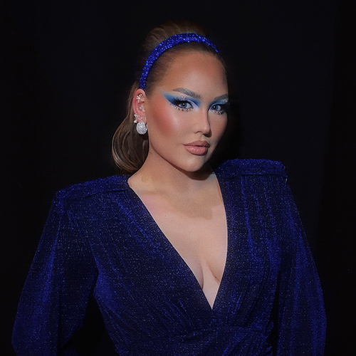 NikkieTutorials poseert in een blauwe glittertop met opvallende oogschaduw en een glinsterende blauwe haarband in haar haar.