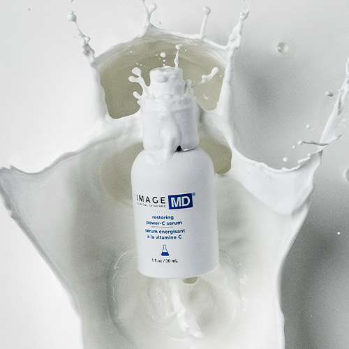 Het IMAGE Skincare MD Restoring Power-C Serum flesje in het midden van een dynamische witte vloeistof splash tegen een lichte achtergrond.