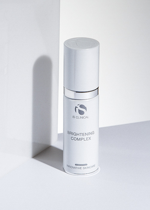 Een flesje iS CLINICAL Brightening Complex staand naast een wit blok in een minimalistische setting.