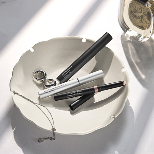De drie producten uit de RevitaLash Spotlight on Lashes collectie liggen decoratief op een elegant wit schaaltje naast een sieraad.