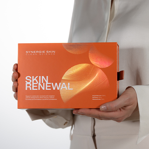 Hand die een oranje Synergie Skin Skin Renewal geschenkdoos vasthoudt