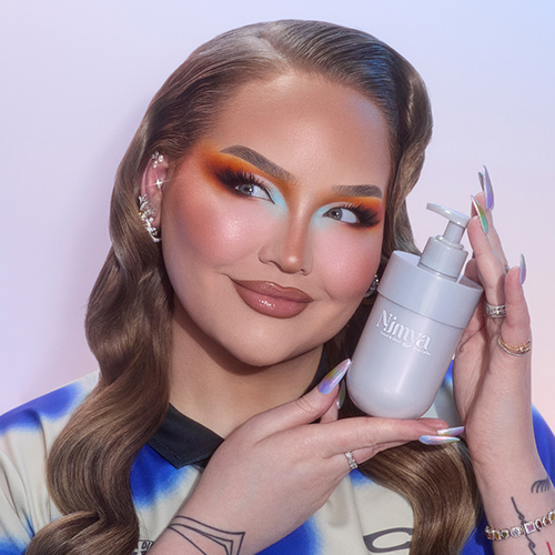 Nikkie de Jager houdt een fles Nimya bodylotion vast en kijkt glimlachmend naar de camera