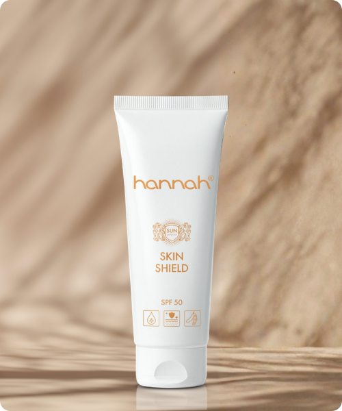 Een staande witte tube hannah Skin Shield SPF50 tegen een rustige achtergrond van beige tinten en abstracte schaduwen van bladeren.