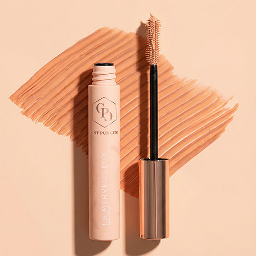 Sfeerbeeld van de Le Merveilleux Lash Primer bovenop een uitgesmeerde textuur (swatch) van het perzikkleurige product.