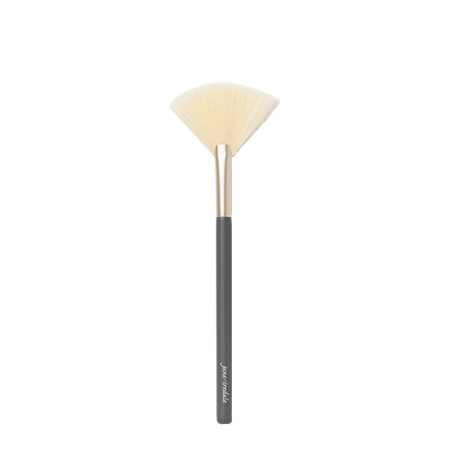 Een Jane Iredale Fan Brush op een witte achtergrond. De kwast heeft een donkergrijze steel met het Jane Iredale logo, een goudkleurige huls en waaier-vormige lichte borstelharen voor een lichte toepassing van poeder of highlighter.
