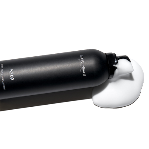 Een liggende zwarte flacon Marc Inbane Shower Foam Numero 9 waar een flinke toef wit doucheschuim uitkomt
