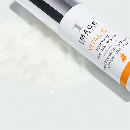 De VITAL C Hydrating Eye Recovery Gel flacon liggend naast een uitgesmeerde hoeveelheid van de witte, hydraterende ooggel.