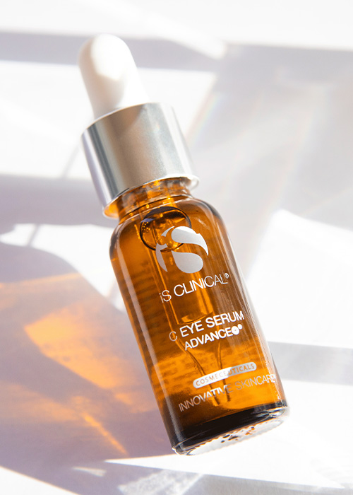 Een flesje iS CLINICAL C Eye Serum Advance op een heldere, reflecterende ondergrond met zonnige schaduwen.