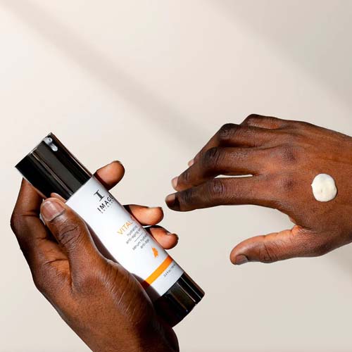 Iemand houdt de flacon van het IMAGE Skincare Vital C serum vast met een druppel product op de rug van de hand.