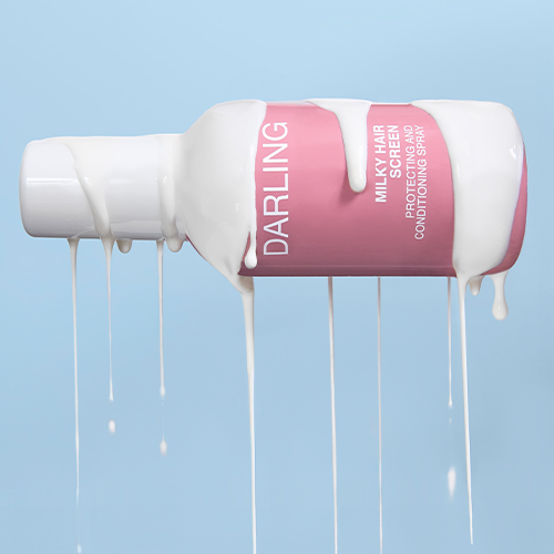 Een roze Darling Milky Hair Screen fles die horizontaal ligt, waar een dikke witte, melkachtige vloeistof overheen druipt tegen een lichtblauwe achtergrond.