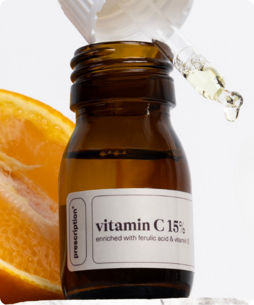 Een bruin glazen flesje vitamine C serum met een pipet erboven en een schijfje sinaasappel ernaast