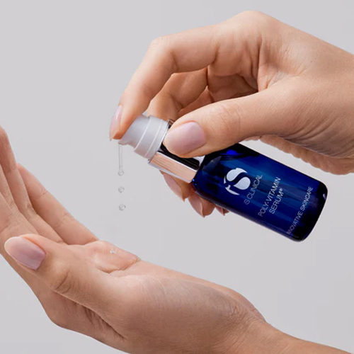 Handen die een helder, vloeibaar serum pompen uit het donkerblauwe flesje van iS Clinical Poly-Vitamin Serum in de handpalm