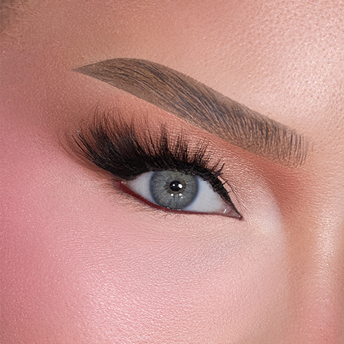 Een close up van het oog van NikkieTutorials met grijze oogkleur, perfect aangebrachte eyeliner en dramatische valse wimpers. De huid is egaal en de wenkbrauw is gestyled.
