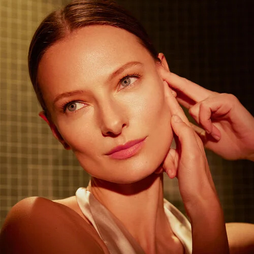 Close-up van een vrouw die met haar vingertoppen haar gezicht aanraakt, ter illustratie van de toepassing van het Natura Bisse Essential Shock Intense Retinol Fluid.