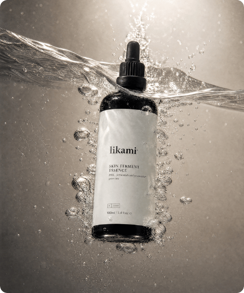 Zwarte fles Likami Skin Ferment Essence ondergedompeld in water met omringende luchtbellen