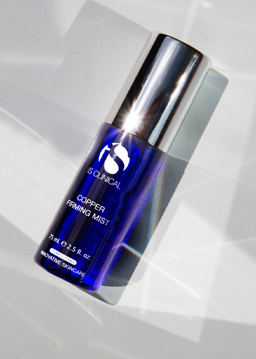 Een flesje iS CLINICAL Copper Firming Mist op een witte, reflecterende ondergrond.