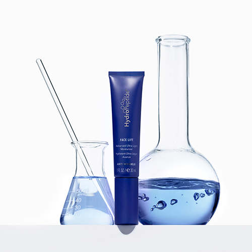 De blauwe tube van de HydroPeptide Face Lift Moisturizer opgesteld tussen glazen laboratoriumkolven en bekers met blauwe vloeistof voor een wetenschappelijke uitstraling.
