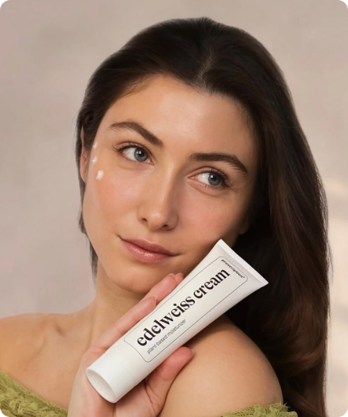 Een vrouw met crème stippen op haar gezicht toont een tube Prescription edelweiss cream