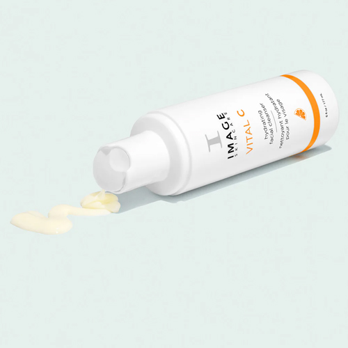 Een IMAGE Skincare VITAL C Hydrating Facial Cleanser flacon liggend op een lichtblauwe achtergrond waarbij een kleine hoeveelheid van de romige cleanser uit de dop komt.