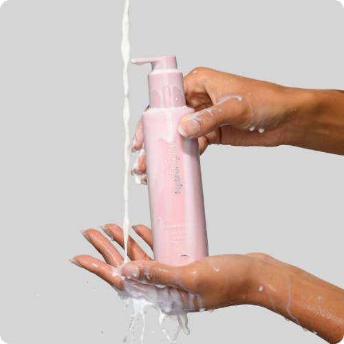 Handen die een roze flacon HydroPeptide Cashmere Cleanse vasthouden terwijl er een romige, melkachtige reiniger over de handen stroomt.