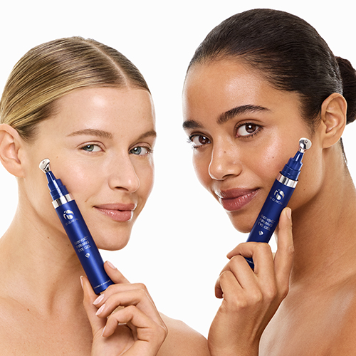 Twee lachende vrouwen houden de blauwe iS Clinical Genexc Firming Eye Gel flacon bij hun gezicht en tonen de metalen applicator roller