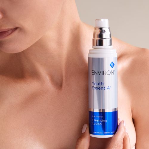Een sfeerbeeld waarin een vrouw de Environ Youth EssentiA Hydra-Intense Cleansing Lotion flacon vasthoudt tegen haar hals en schouder.