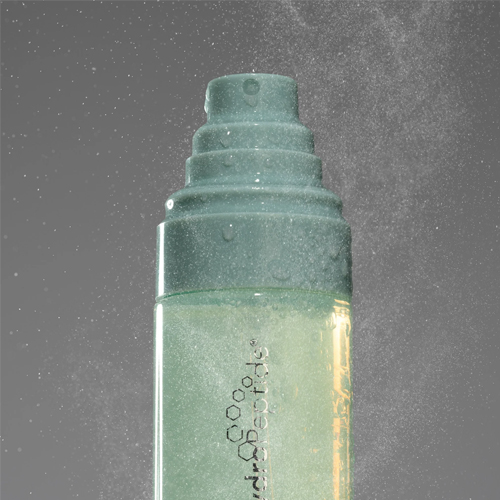 Close up van de verstuiver van de HydroPeptide HydraFlora Mist die een fijne nevel spuit tegen een grijze achtergrond met sfeervolle verlichting.