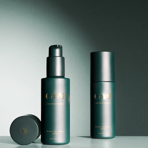 Twee luxe donkergroene flacons van EAVE I AM PROTECTING Mineral Sun Cream SPF50 met gouden letters op een lichte ondergrond waarvan één fles is geopend