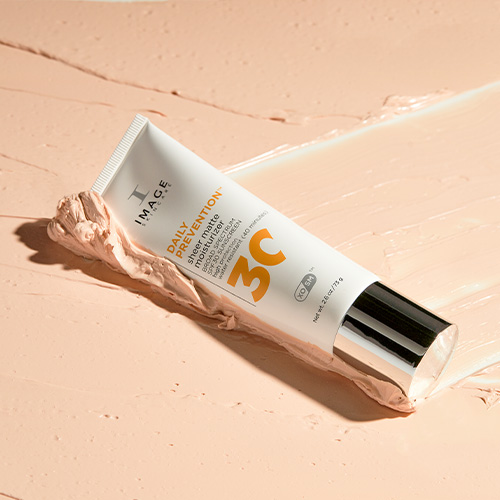 De witte tube van de Sheer Matte Moisturizer rustend op een dikke laag van de beige-kleurige crème textuur.