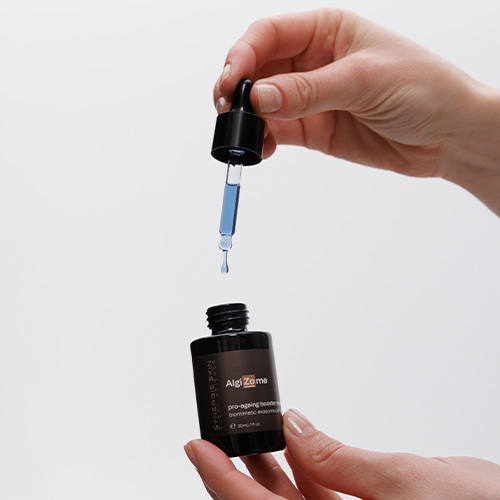 Iemand houdt de AlgiZome flacon vast terwijl de druppelaar een blauwe vloeistof omhoog haalt, wat de textuur van het serum laat zien.