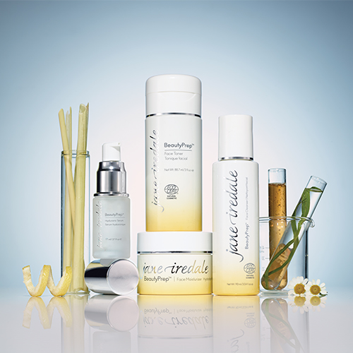 Een groepsfoto van de volledige jane iredale BeautyPrep collectie inclusief cleanser, toner, moisturizer en serum, omringd door botanische ingrediënten in reageerbuisjes.