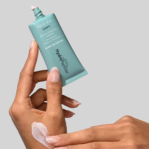 Hand van een model toont de roze textuur van het HydroPeptide Balancing Mask op de handrug naast een tube
