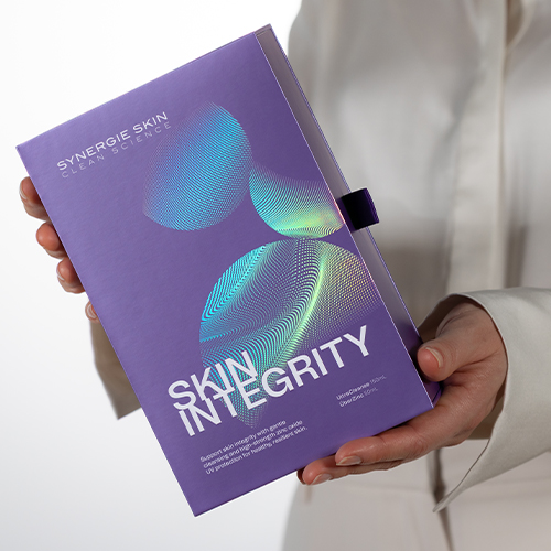 Hand die een paarse Synergie Skin Integrity geschenkdoos presenteert