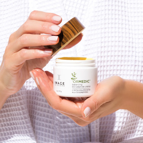 Een model haalt dop van pot af van de IMAGE Skincare ORMEDIC Bio-Peptide Crème aan op de huid voor een gezonde balans.