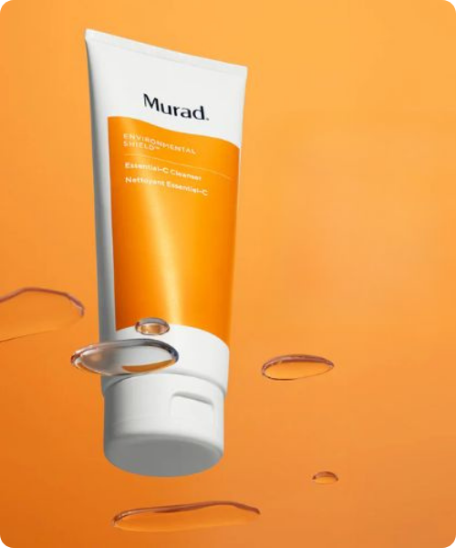 Een tube Murad Essential C Cleanser op een oranje achtergrond omringd door waterdruppels
