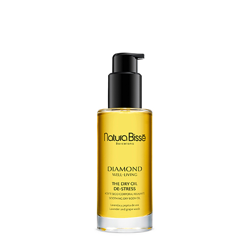 Een glazen flacon van 100ml Natura Bissé Diamond Well Living De-Stress Dry Body Oil met een zwarte pompdispenser. De olie heeft een warme gouden kleur.