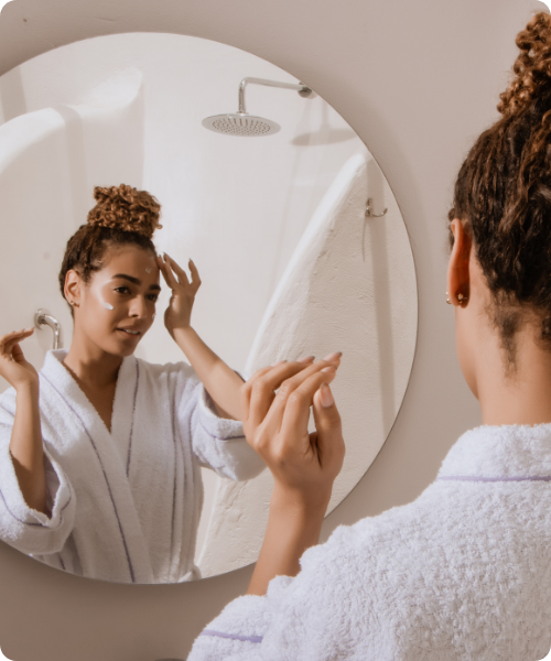 vrouw met haar in knot brengt hannah crème aan voor de spiegel
