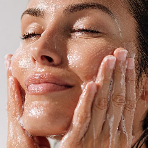 Een vrouw met gesloten ogen wast haar gezicht met schuimende cleanser