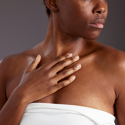 Een detailopname van een model dat met de hand over de hals en het decollete strijkt om een huidverzorgingsproduct zoals de UberZinc Body lotion aan te brengen tegen een grijze achtergrond.