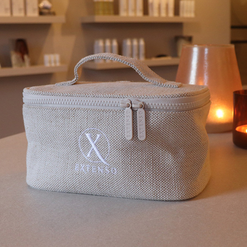 Een sfeerbeeld van de beige Extenso everyday beautycase op een tafel in een salon-omgeving met warme verlichting.