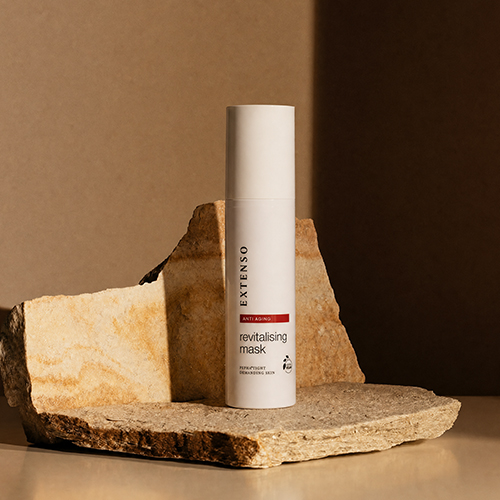 Een witte fles Extenso revitalising mask staand op een ruwe beige steen met sfeervolle schaduwen