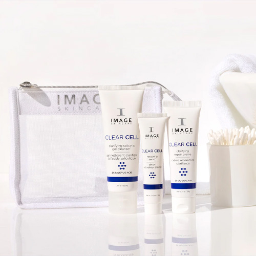 De IMAGE Skincare CLEAR CELL set opgesteld op een witte tafel naast een bakje met wattenstaafjes en een witte handdoek, wat een schone badkameruitstraling geeft.