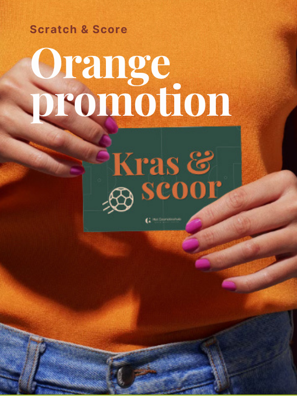 Twee handen met roze nagellak houden een groene kraskaart met de tekst 'Kras & scoor' vast tegen een achtergrond van een oranje trui en spijkerbroek.