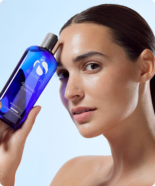 Een vrouw die een blauwe fles iS Clinical Cleansing Complex tegen haar gezicht houdt