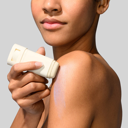 Een model brengt de Sun Slick SPF 50 stick aan op de schouder wat een subtiele glans achterlaat op de huid.