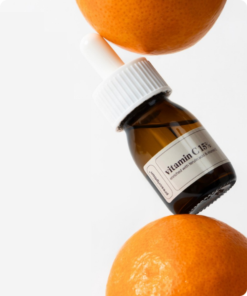 Een bruin glazen flesje met wit pipet en een Prescription label voor vitamin c 15% dat subtiel geplaatst is tussen twee verse sinaasappels tegen een heldere achtergrond.