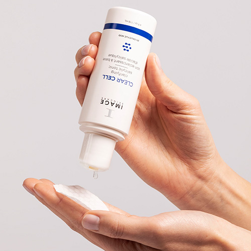Handen die de IMAGE Skincare Clear Cell Salicylic Tonic op een wattenschijfje druppelen voor gebruik.