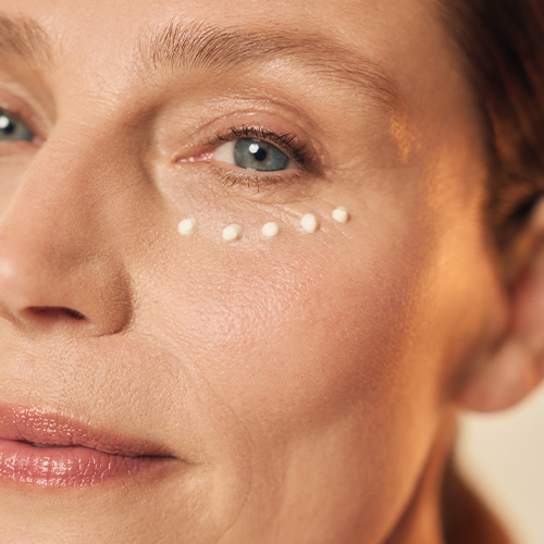 Een vrouw met kleine stipjes oogcrème aangebracht onder haar oog, klaar om in de huid te worden gemasseerd.